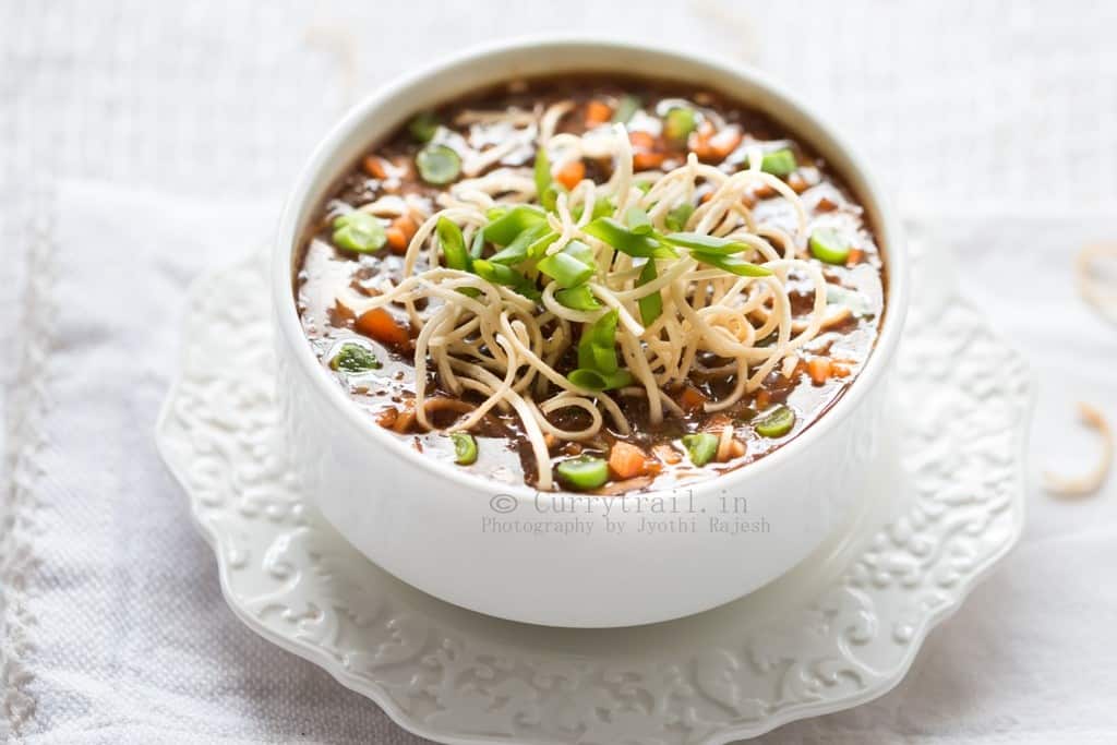 hot sour and spicy vegetable manchow soup topped with crunchy fried noodles served in white bowl