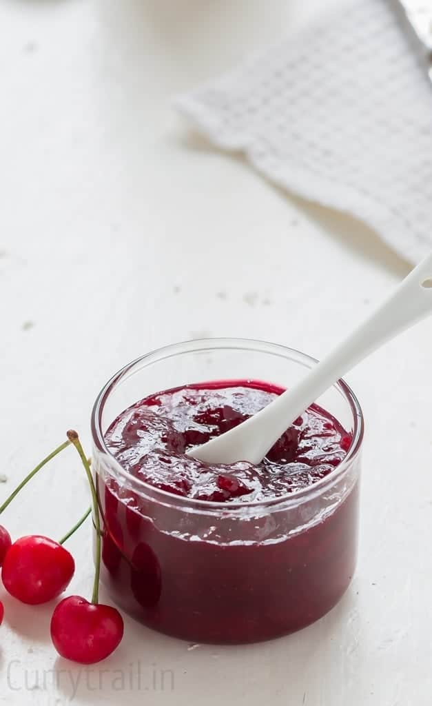 A jar of fresh homemade cherry jam with fresh cherries on side