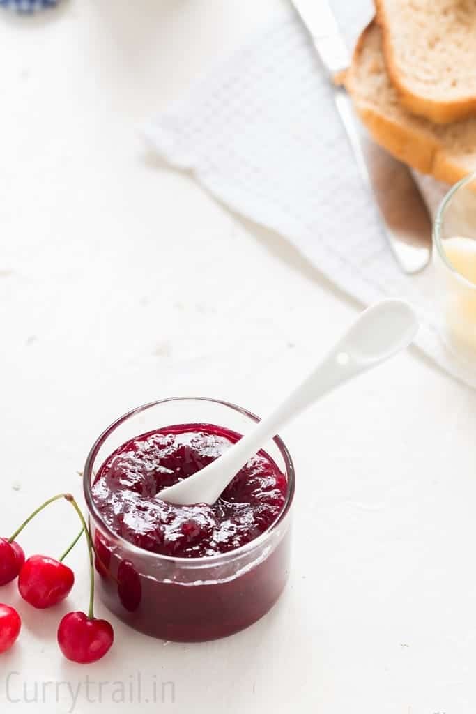 homemade cherry jam with white ceramic spoon and bread slices on the sides