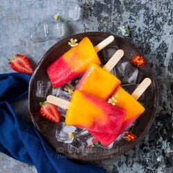 4 strawberry mango popsicles placed on round metal tray with ice cubes and pretty flowers on it