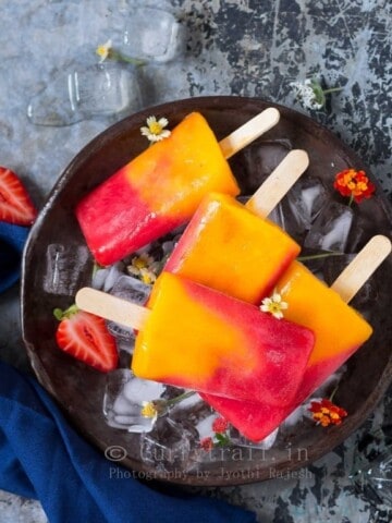 4 strawberry mango popsicles placed on round metal tray with ice cubes and pretty flowers on it