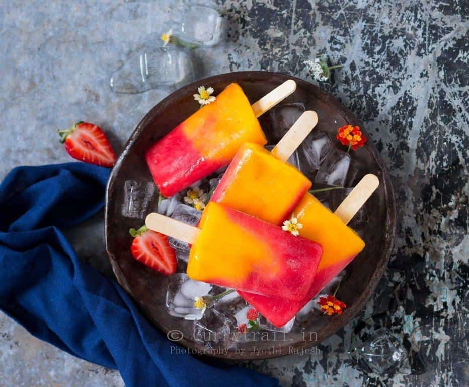 4 strawberry mango popsicles placed on round metal tray with ice cubes and pretty flowers on it