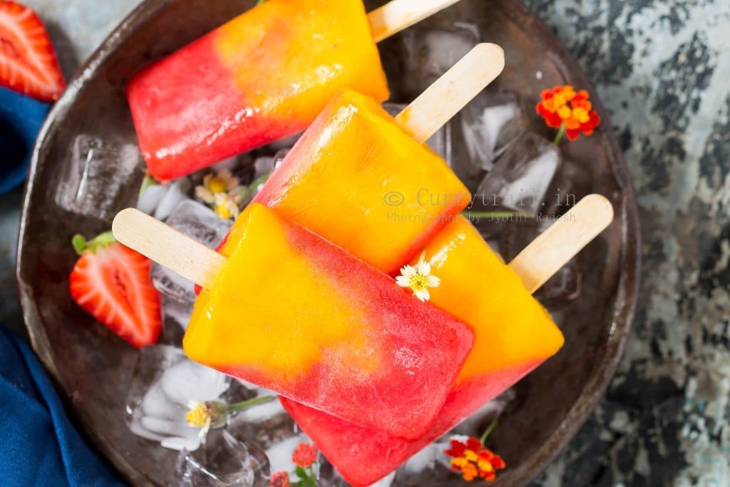 Close view of 2 ingredients strawberry mango popsicles over ice cubes on a round plate