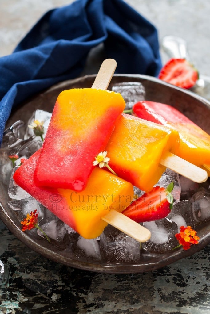 strawberry mango popsicles with fresh cut strawberries placed on ice cubes in a plate