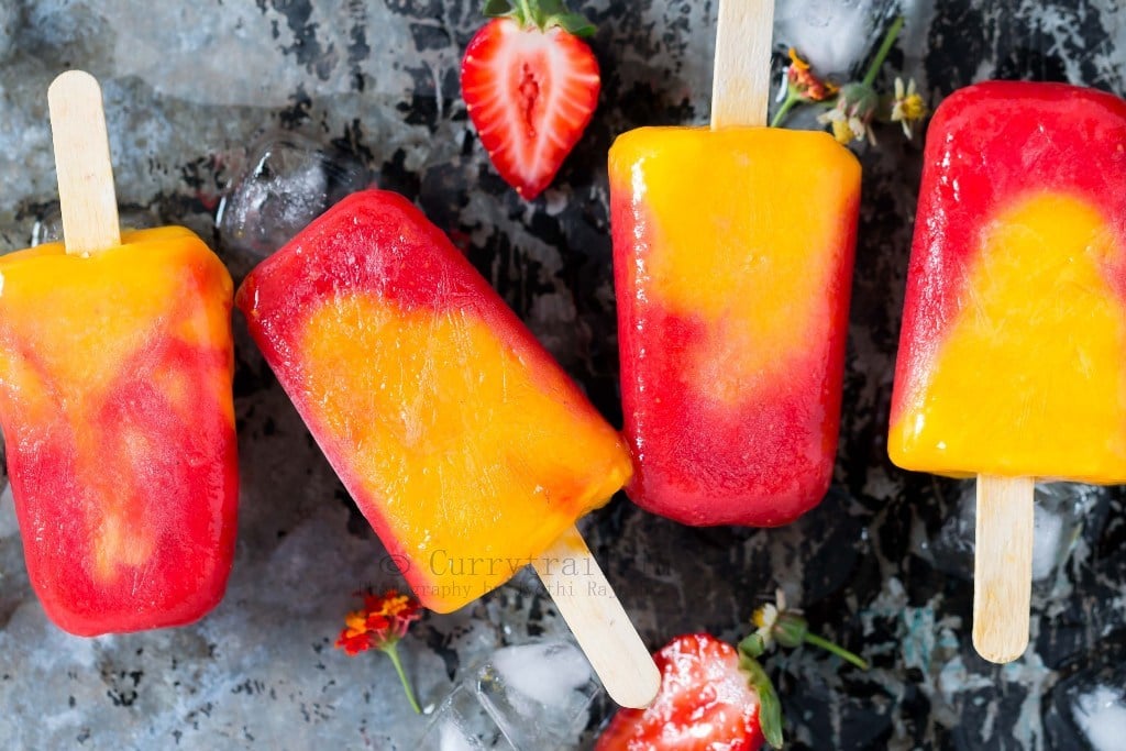 4 strawberry mango popsicles lined on a rustic metal plate with ice cubes