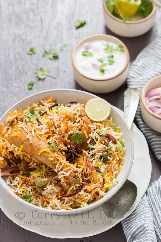 chicken dum biryani in ceramic bowl with raita on side