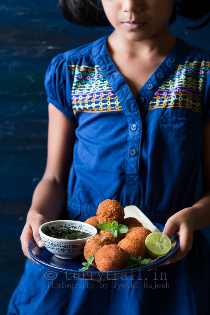 Little girl holding a blue plate full of cheese stuffed garlic chicken balls along with mint sauce