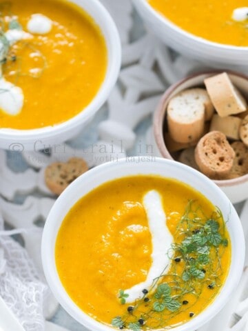 3 white bowls of roasted carrot soup served on white tray with roasted bread on side