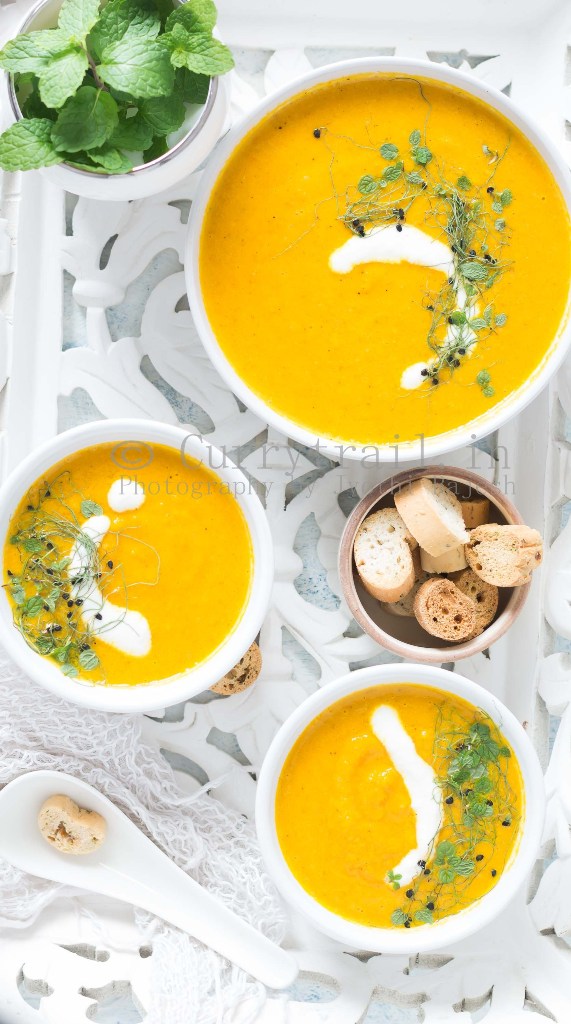 roasted carrot soup served in white bowl with roasted bread on side