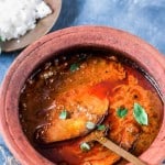 Kerala fish curry in a clay pot with a spatula.