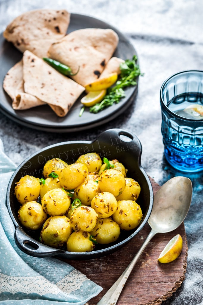 Jeera aloo in black cast iron pan with rotis on side and a glass of water