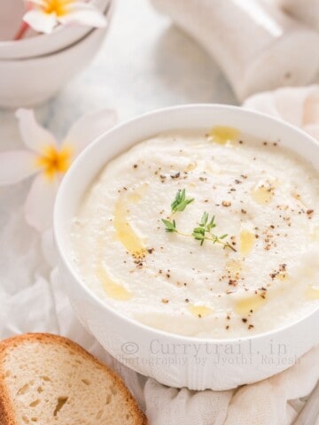 creamy cauliflower soup serve in white bowl with crusty bread on side