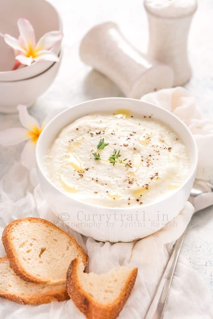 cream of cauliflower soup served in white bowl with crusty bread on sides