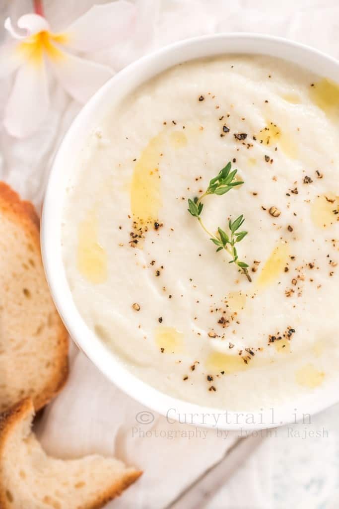 creamy cauliflower soup serve in white bowl with crusty bread on side