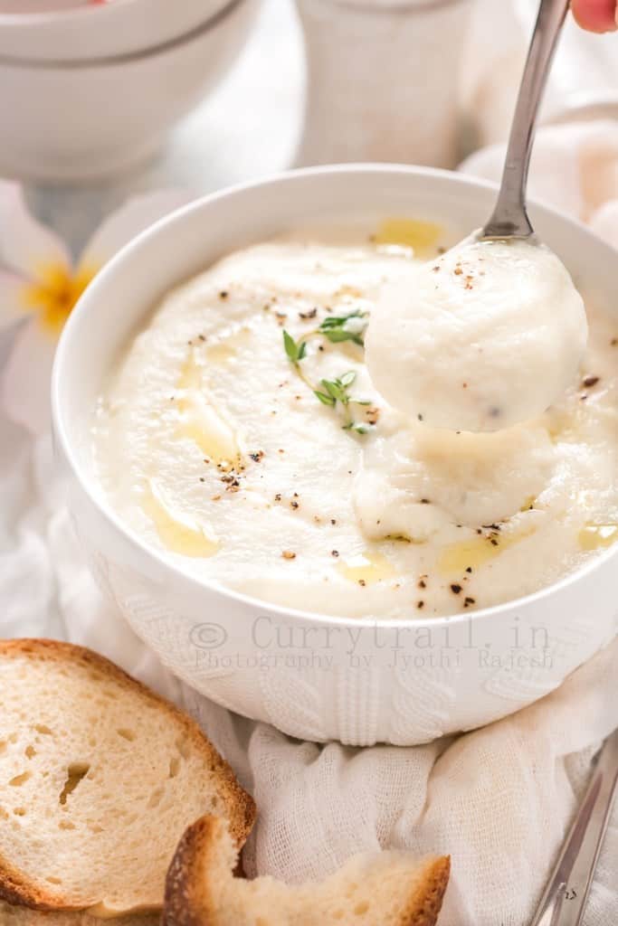 spooning out cream of cauliflower soup from white bowl