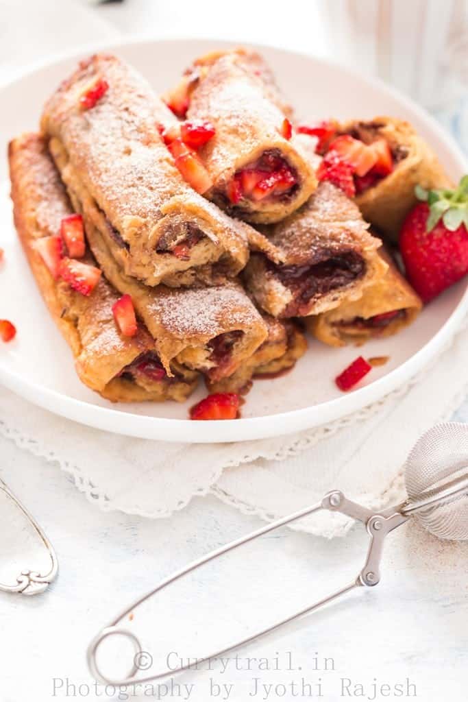 A plate full of Nutella Strawberry French toast Roll Ups with fresh strawberries on side