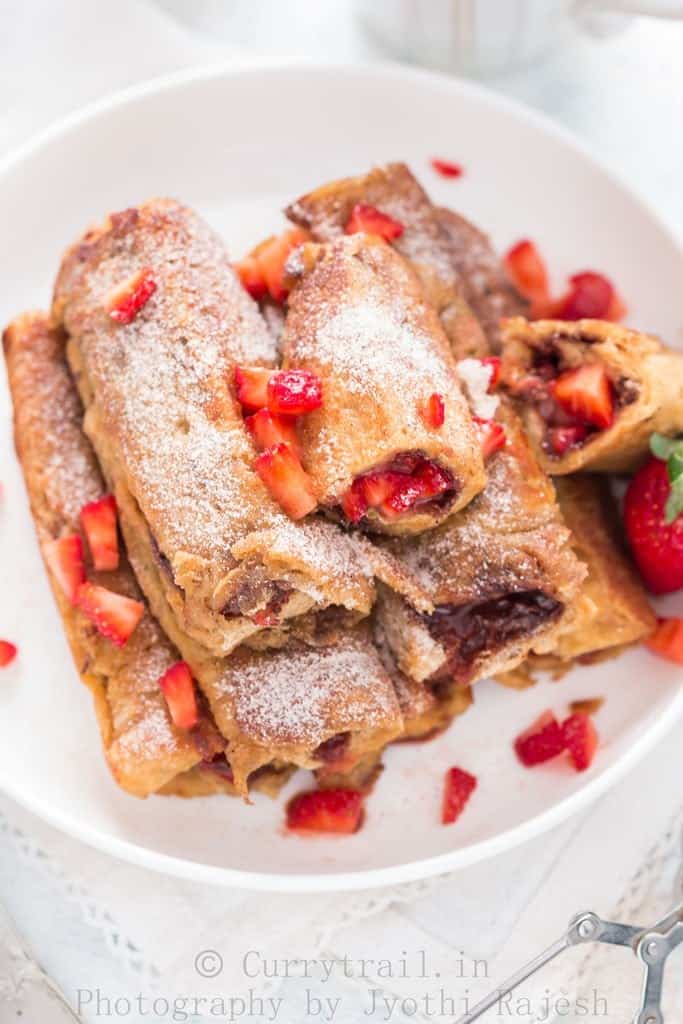 French toast roll ups with Nutella and strawberries stacked on a white plate 