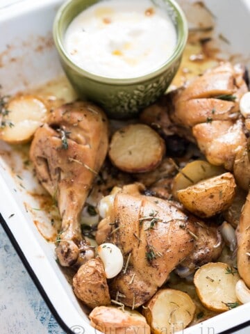 Lebanese style baked chicken and potatoes served in white enamel plate with garlicky sauce on the side