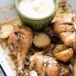 Lebanese style baked chicken and potatoes served in white enamel plate with garlicky sauce on the side with text overlay