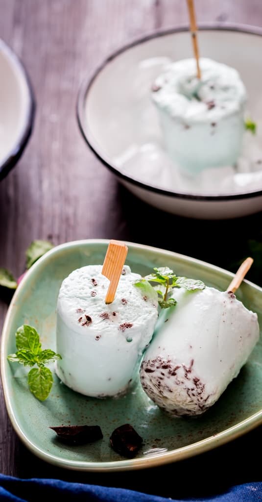 2 chocolate mint popsicles on triangular shaped plate with fresh mint leaves on sides