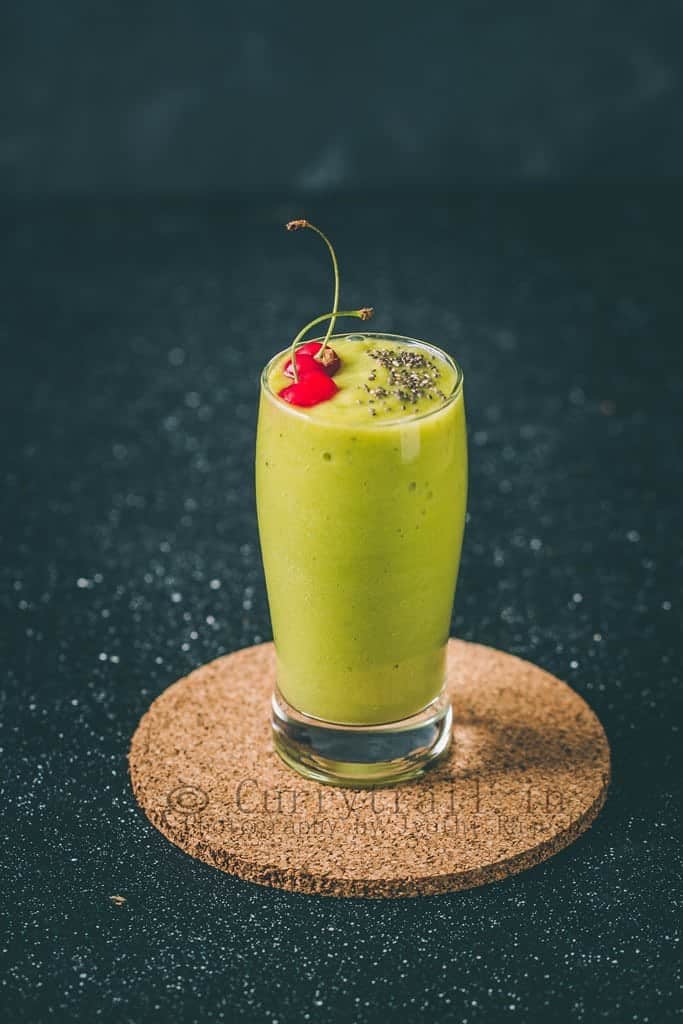 A glass full of avocado banana smoothie with chia seed and cherries