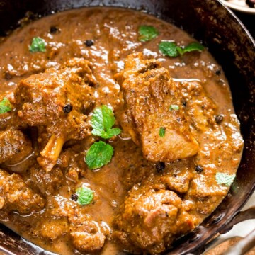 spicy pepper mutton curry served in cast iron pan with spoon on the side