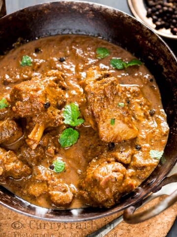 spicy pepper mutton curry served in cast iron pan with spoon on the side