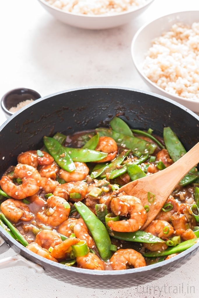 stir fried shrimp cooked in skillet with rice bowl on sides