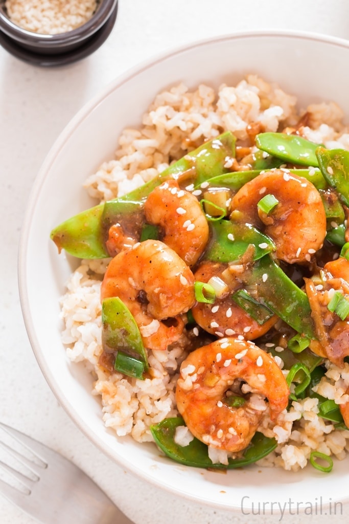 close up view of shrimp and snow peas stir fry served over rice in bowl