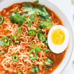 Soft boiled egg placed over a bowl of spicy sriracha ramen noodle soup in white bowl