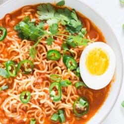 Soft-boiled egg placed over a bowl of spicy sriracha ramen noodle soup in a bowl.