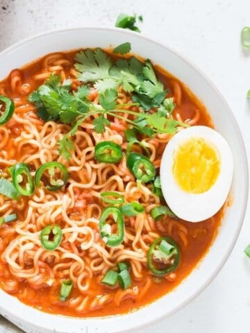 Soft boiled egg placed over a bowl of spicy sriracha ramen noodle soup in white bowl