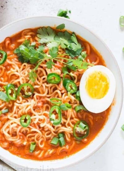 Soft boiled egg placed over a bowl of spicy sriracha ramen noodle soup in white bowl