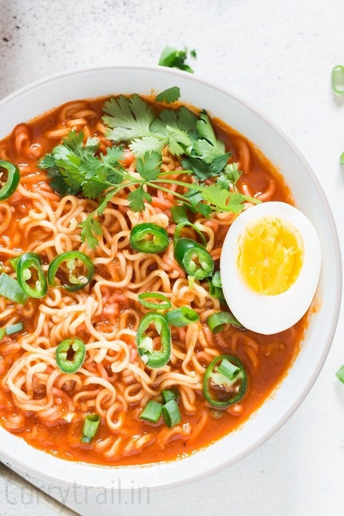 Soft boiled egg placed over a bowl of spicy sriracha ramen noodle soup in white bowl