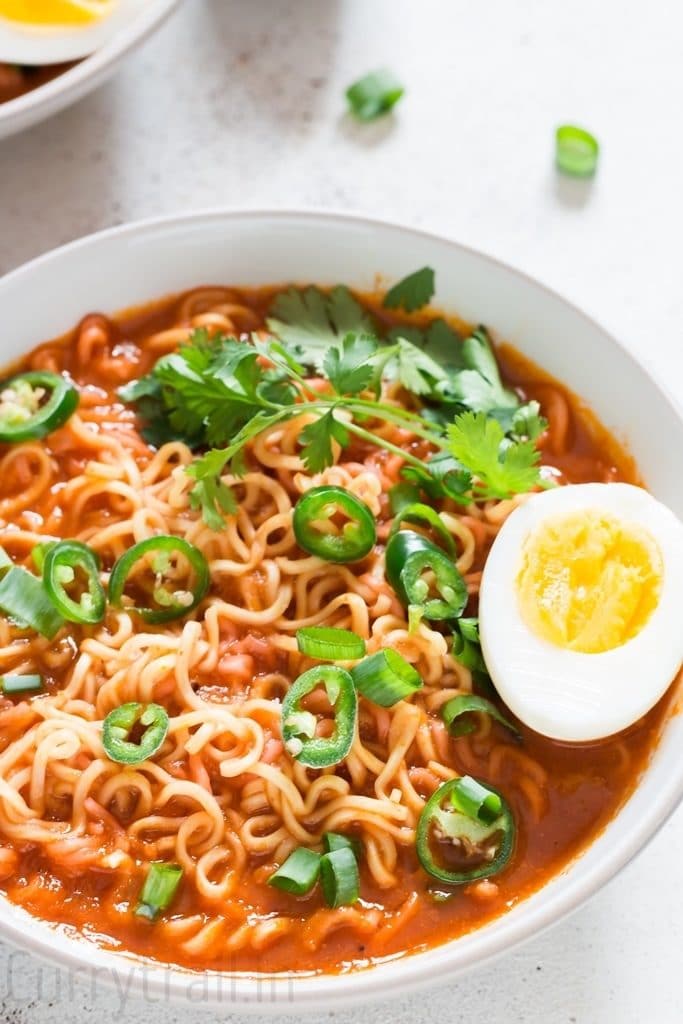 spicy sriracha ramen noodles soup with soft boiled egg in a white bowl