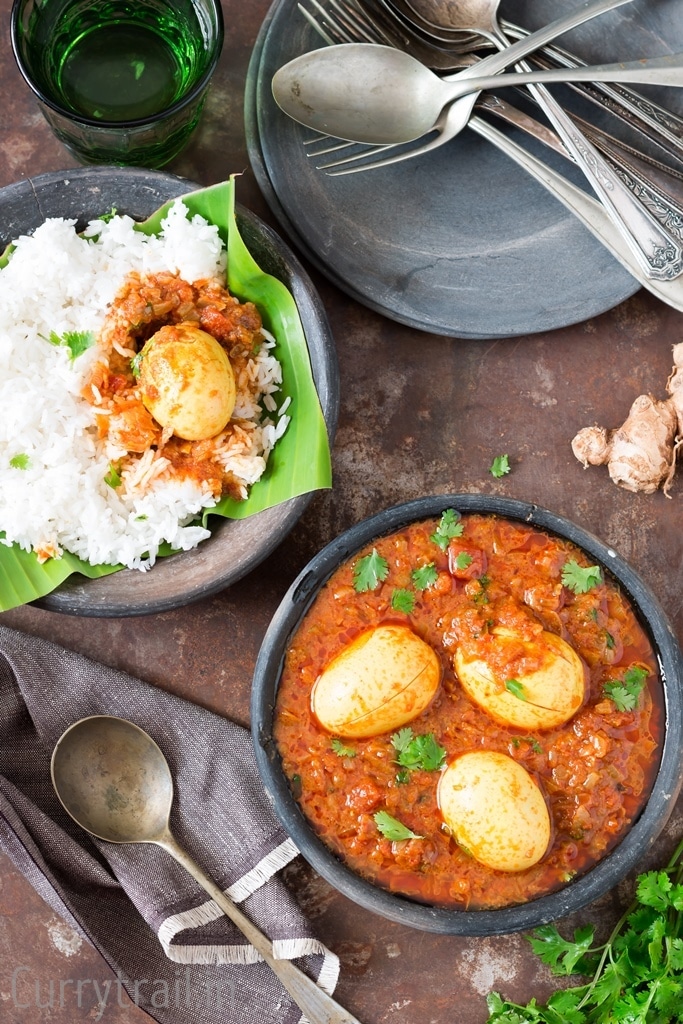 A black bowl with south Indian spicy egg curry with a bowl of rice and curry on top