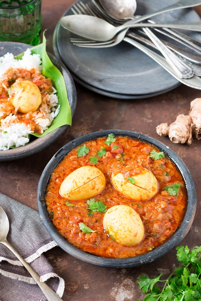 Two black bowls with South Indian spicy egg curry and rice in the background