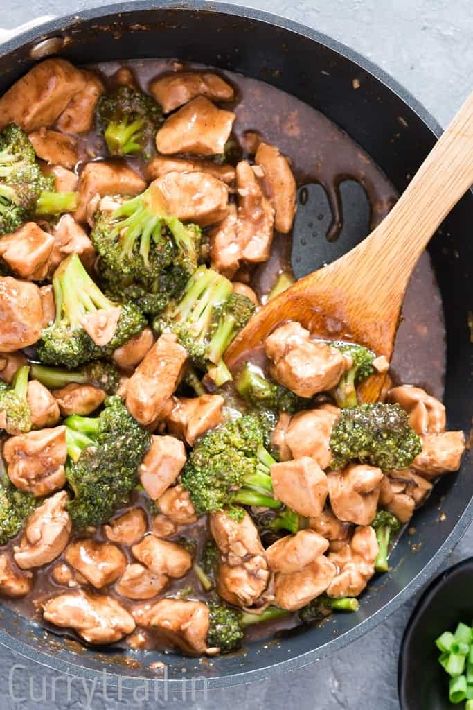 Chicken and broccoli stir fry dish in a skillet with a wooden spoon