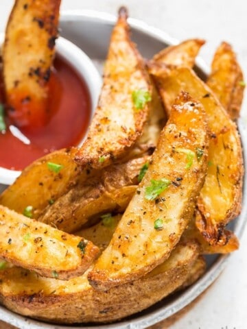 A plate with Crispy Garlic Parmesan Baked Potato Wedges and a small bowl of ketchup on side