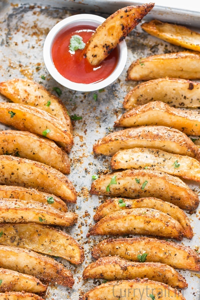 Baking tray with Crispy Garlic Parmesan Baked Potato Wedges out of oven ready to be served with ketchup on side