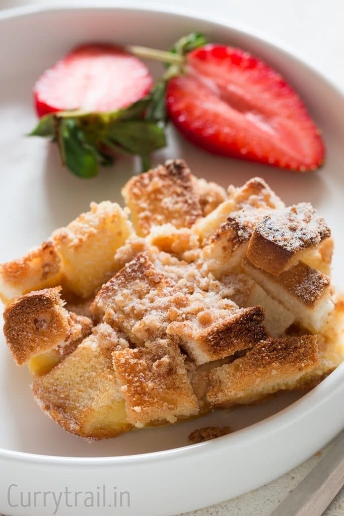 Baked French toast casserole served in a white plate with fresh strawberries on side
