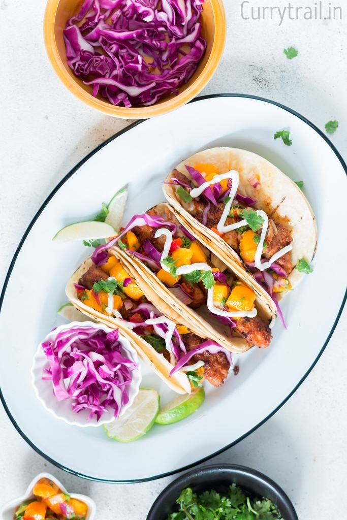 Oval white plate with tilapia fish tacos arranged, purple cabbage in a small bowl