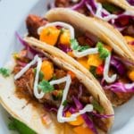 Tilapia fish tacos recipe with white creamy fish taco sauce drizzled on top on a white plate