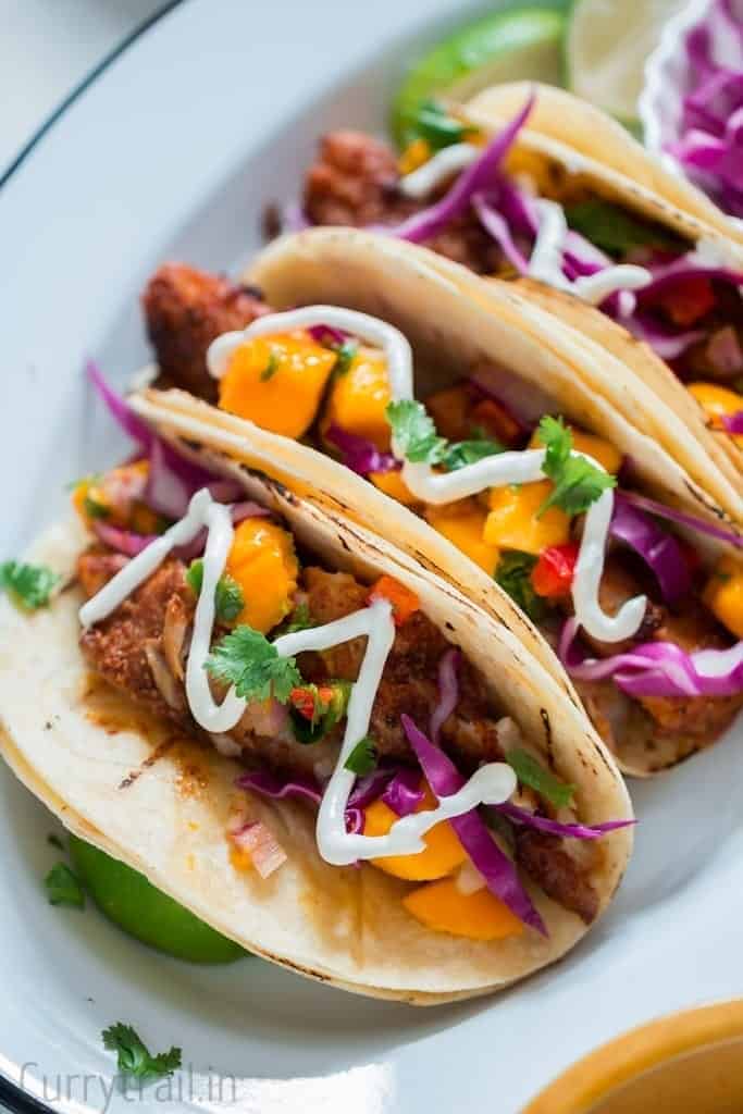 Tilapia fish tacos recipe with white creamy fish taco sauce drizzled on top on a white plate