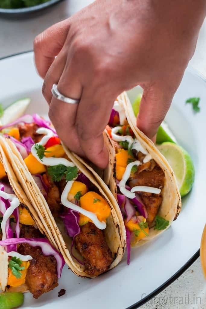 picking a tilapia fish taco placed on a enamel white plate