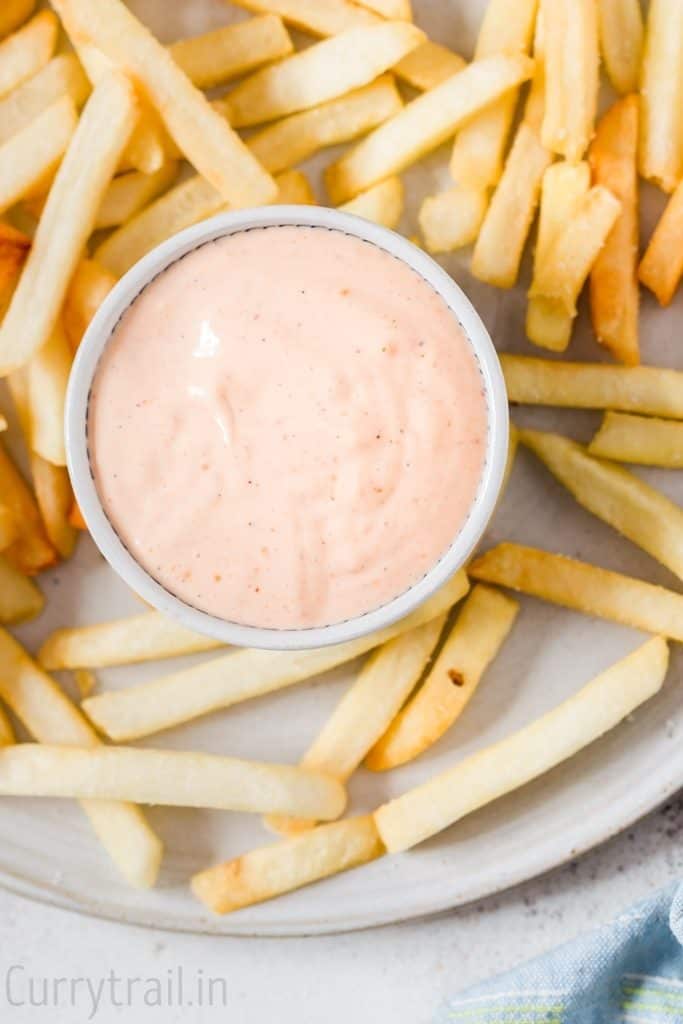 A white plate with potato fries and a small bowl of boom boom sauce