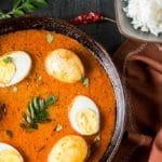 Chettinad egg curry served in pan with curry leaves on side and a bowl of rice