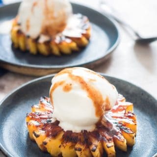 Grilled pineapple topped with vanilla ice cream on blur plate