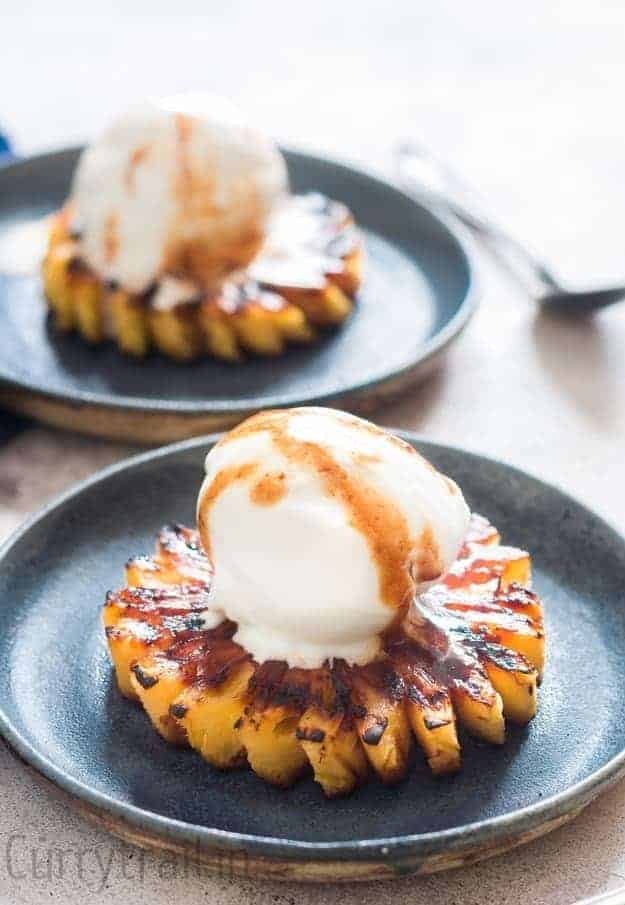 Grilled pineapple topped with vanilla ice cream on blur plate