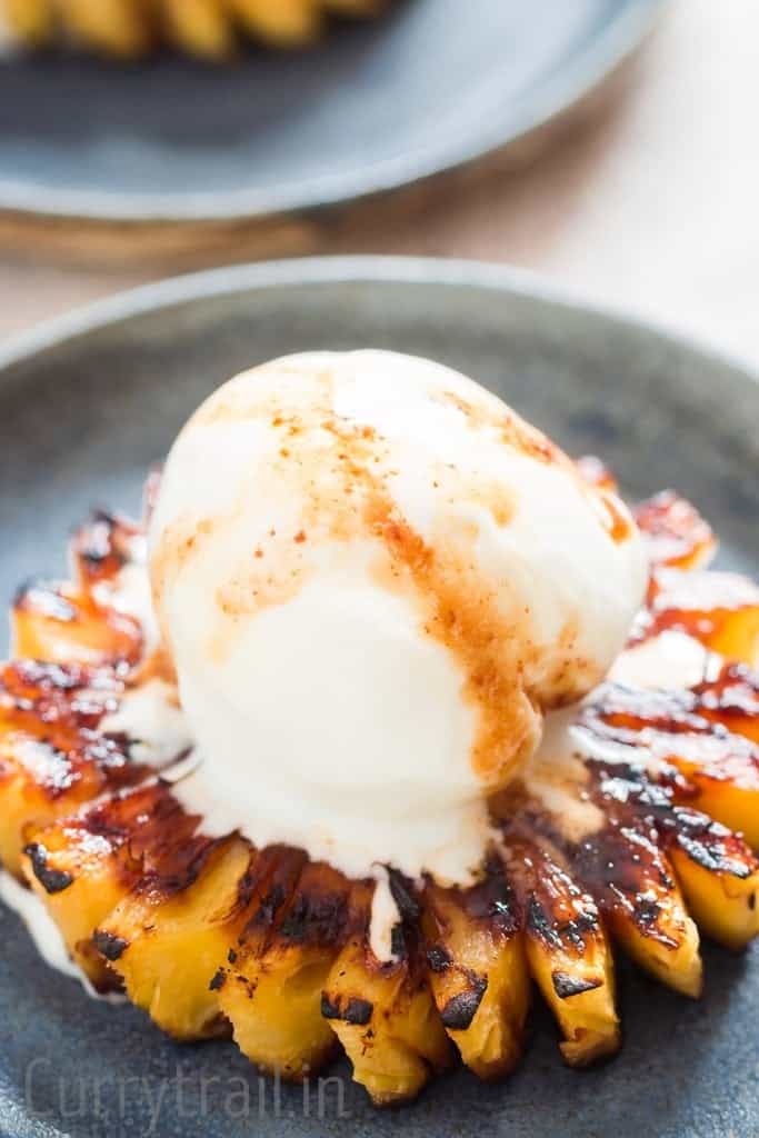 A scoop of vanilla ice cream over grilled pineapple on blue plate
